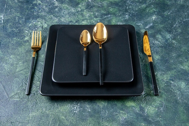 front view dark plates with golden spoons fork and knife on dark blue background