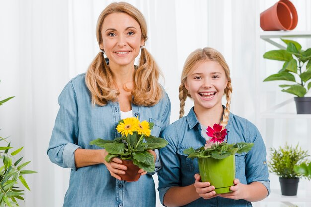 Вид спереди дочь и мама с цветами в руках горшок