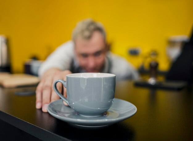 Front view of defocused barista looking at cup of coffee
