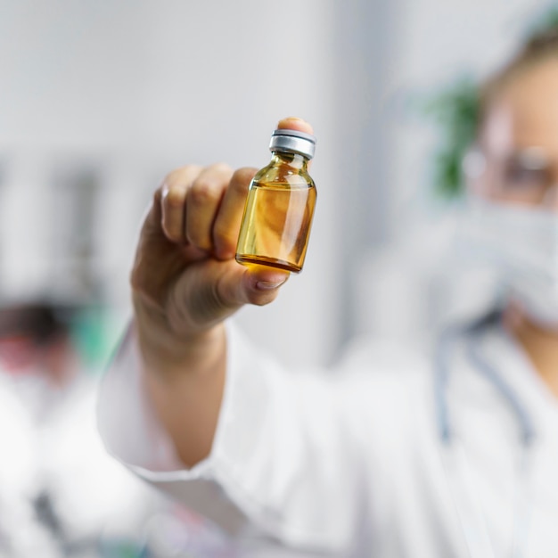 Front view of defocused female researcher with vaccine bottle