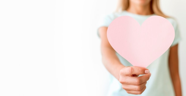 Free photo front view of defocused woman holding heart shape with copy space