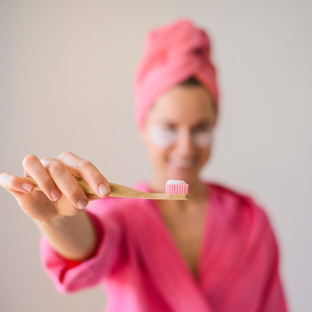 Front view of defocused woman with eye patches holding toothbrush