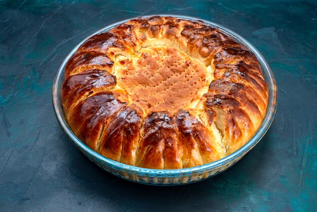 Вид спереди восхитительный испеченный торт круглой формы сладкий внутри стеклянной сковороды на голубом фоне.