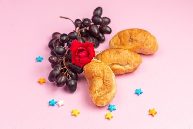 Front view delicious baked croissants with fruit filling along with fresh black grapes on pink desk