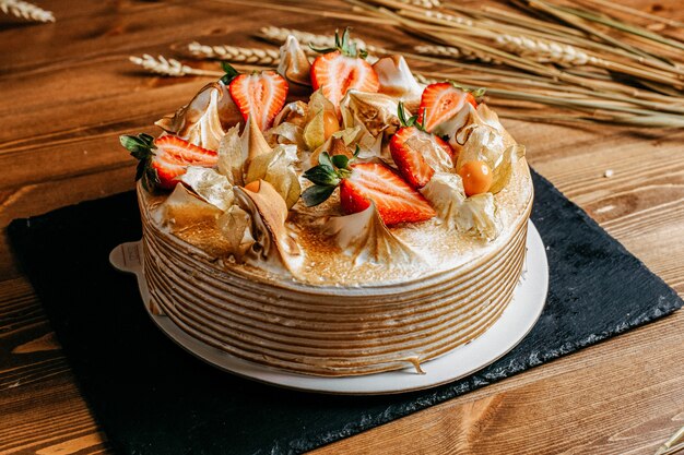 Вид спереди вкусный торт ко дню рождения украшенный вкусной клубникой круглый внутри белой тарелки сладкое печенье на день рождения на коричневом фоне