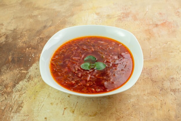 Front view delicious borsch red ukrainian beet soup inside plate on light-brown surface