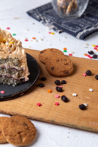 Вид спереди вкусного кусочка торта внутри темной тарелки со свечами печеньем и маленькими знаками зодиака на светлом столе