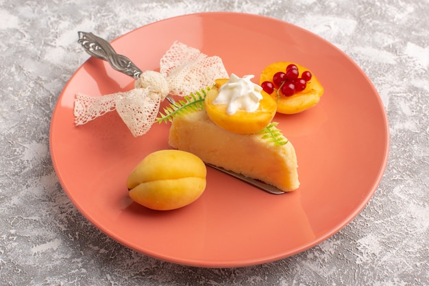 Front view of delicious cake slice with cream and fresh apricots inside pink plate on the light desk
