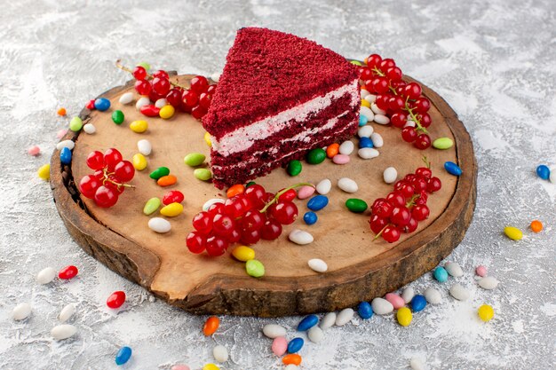 Front view of delicious cake slice with cream and fruits on the wooden desk with colorful candies