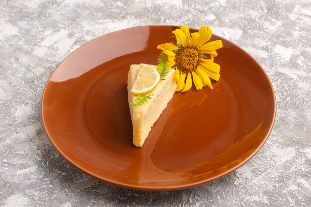 Front view of delicious cake slice with lemon inside brown plate on the light desk