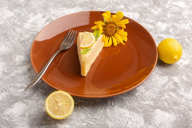 Front view of delicious cake slice with lemon inside brown plate on the light surface