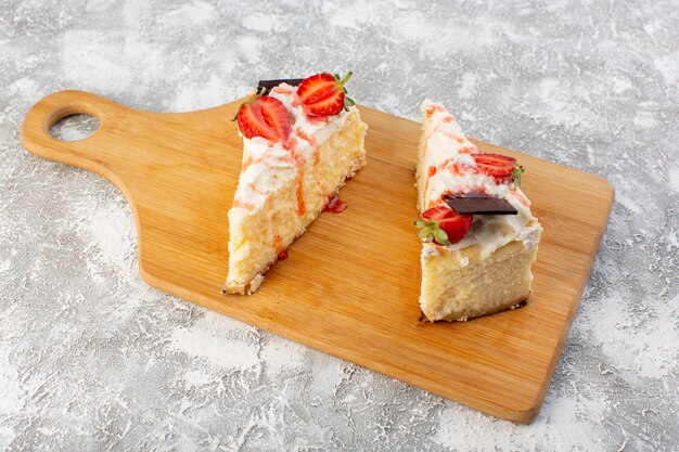 Front view of delicious cake slices with chocolate cream and strawberry on the light surface