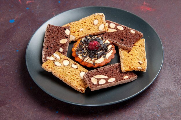 Вид спереди вкусные кусочки торта с орехами и маленьким печеньем на темном пространстве