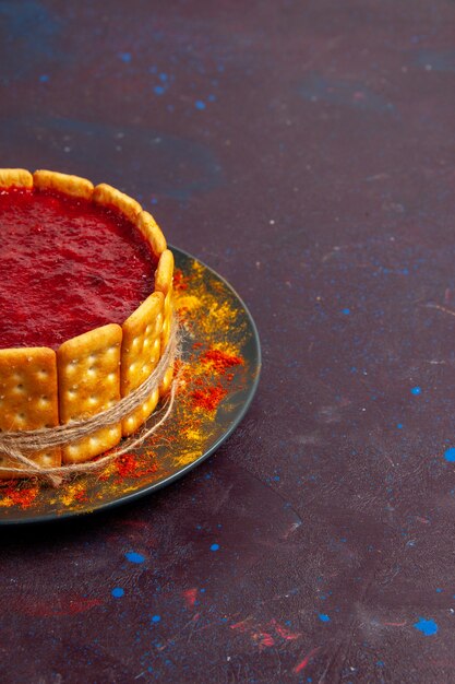 Front view delicious cake with red cream and cracker cookies on dark desk biscuit cake sugar dessert pie sweet cookie