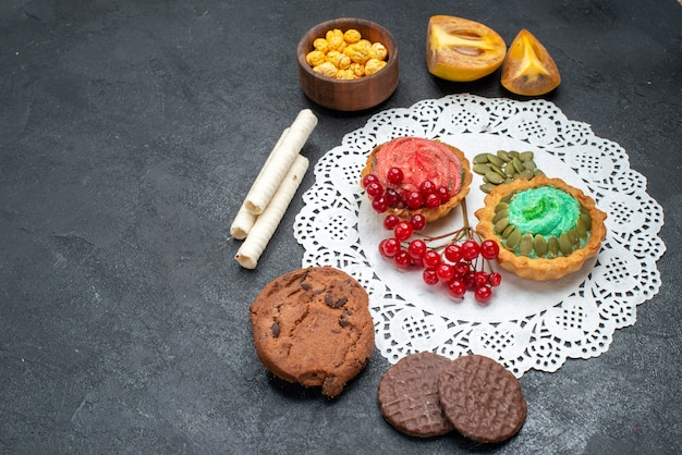 Vista frontale deliziose torte con biscotti e frutta su sfondo scuro