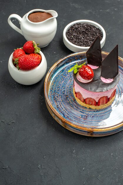 Вид спереди вкусный чизкейк с клубникой и шоколадом на овальных тарелках с клубникой в шоколаде на темном
