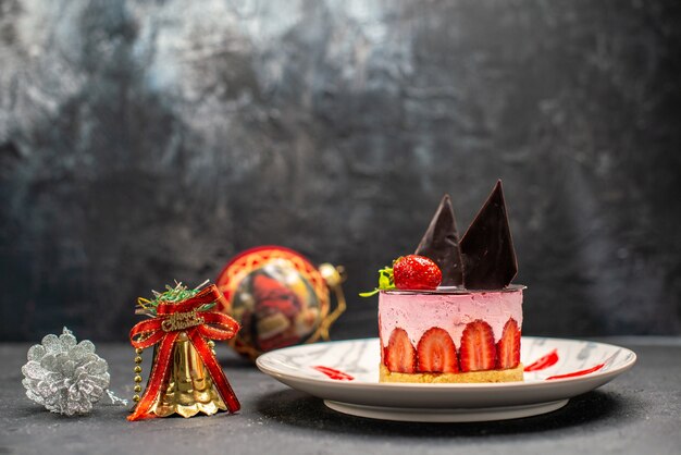 Front view delicious cheesecake with strawberry and chocolate on oval plate xmas tree toys on dark free space