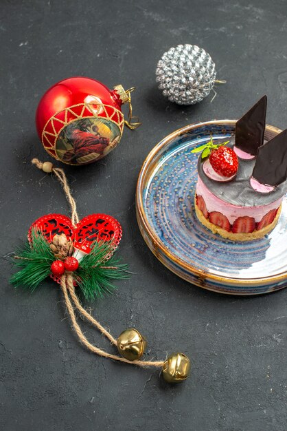 Front view delicious cheesecake with strawberry and chocolate on oval plate xmas tree toys on dark isolated background