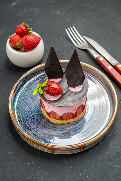 Front view delicious cheesecake with strawberry and chocolate on plate bowl with strawberries fork and knife on dark