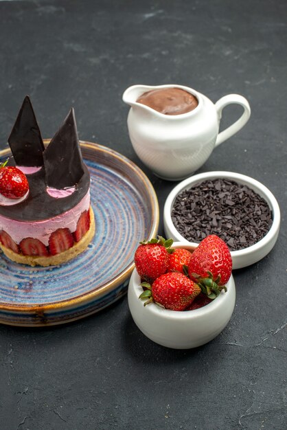 Free photo front view delicious cheesecake with strawberry and chocolate on plate bowls with chocolate strawberries dark chocolate on dark isolated background