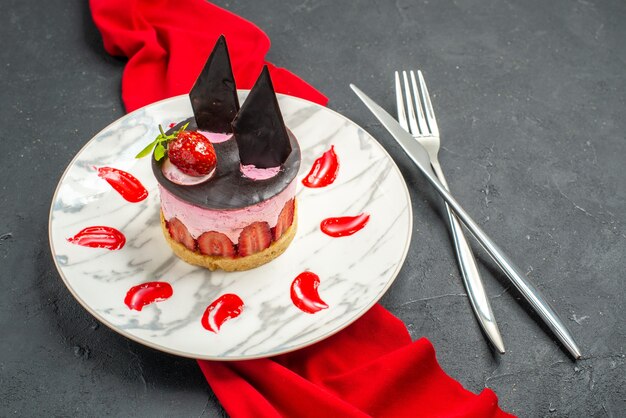 접시에 딸기와 초콜릿을 곁들인 맛있는 치즈케이크 전면 보기 빨간색 목도리를 교차 나이프와 포크를 어둠 속에서