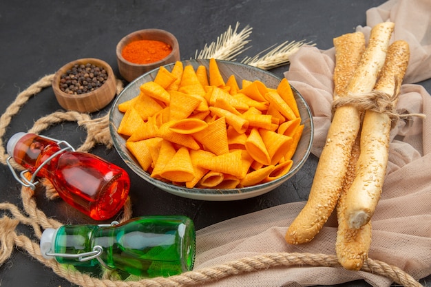 Front view of delicious chips fallen bottles peppers on towel and rope on a black background