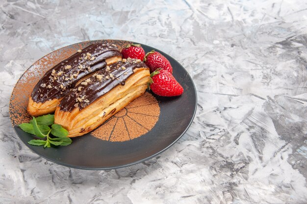 Foto gratuita vista frontale deliziosi bignè al cioccolato con fragole su un dolce dolce da scrivania leggero