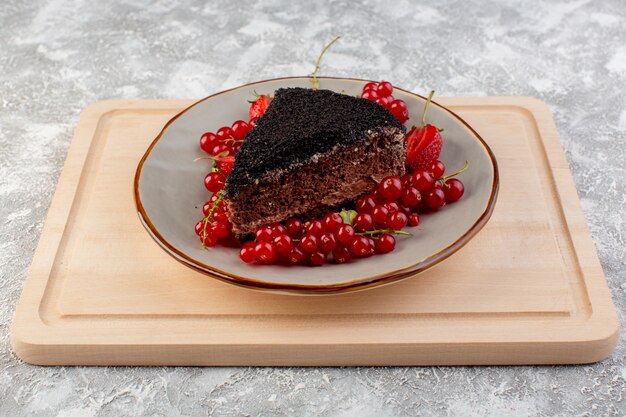 木製の机の上のチョコクリームと新鮮な赤いクランベリーでスライスしたおいしいチョコレートケーキの正面図