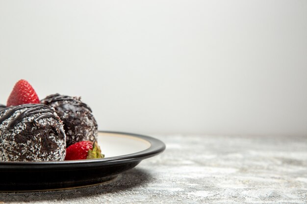 Вид спереди вкусные шоколадные пирожные со свежей красной клубникой на светло-белой поверхности шоколадный сахарный бисквит, выпечка сладкого торта