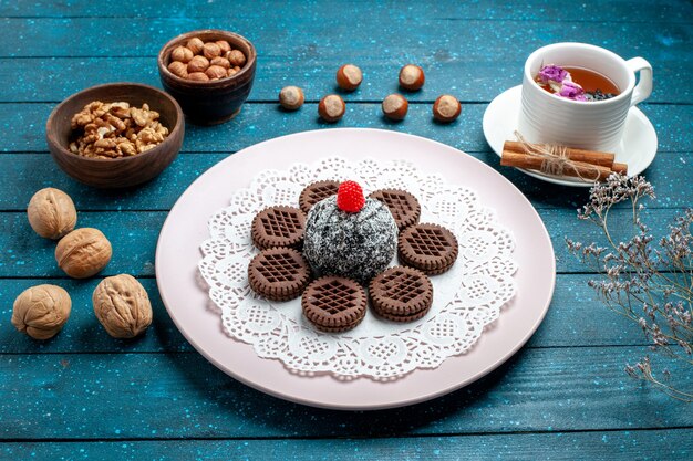 Front view delicious chocolate cookies with nuts and cup of tea on blue rustic desk biscuit tea cookie sweet cake sugar