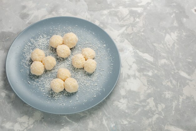 Вид спереди вкусных кокосовых конфет внутри синей тарелки на белой стене
