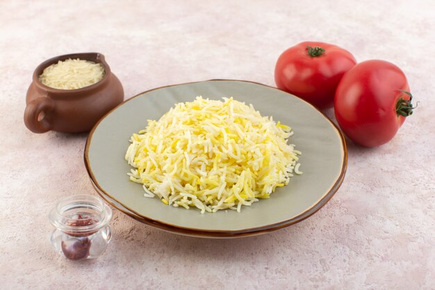 A front view delicious cooked rice inside plate along with fresh red tomatoes on the pink desk food meal vegetable rice