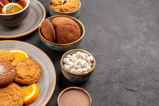 Front view delicious cookies with cup of tea and sliced oranges on dark background biscuit fruit sweet cake cookie citrus