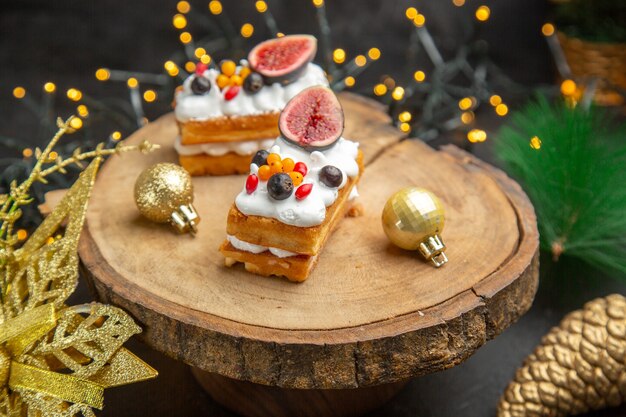 Front view delicious cream cakes around new year tree toys on dark background cake sweet photo cream dessert
