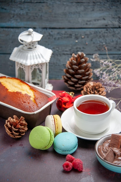 Вид спереди вкусные французские макароны с шоколадом и чашкой чая на темном фоне пирог, бисквит, сладкий чай, торт, печенье