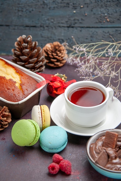 Front view delicious french macarons with chocolate and cup of tea on a dark background tea drink pie biscuit cake cookie