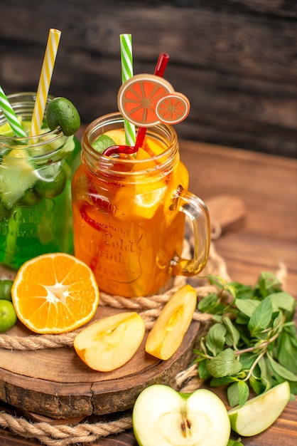 Front view of delicious fresh juices and fruits on a wooden tray on a brown background