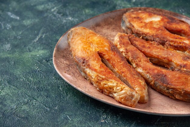 Front view of delicious fried fish on a brown plate on the left side on mix colors table with free space