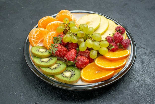 Vista frontale deliziosa composizione di frutta fresca affettata e frutta dolce sullo sfondo scuro dieta salutare fresca e matura