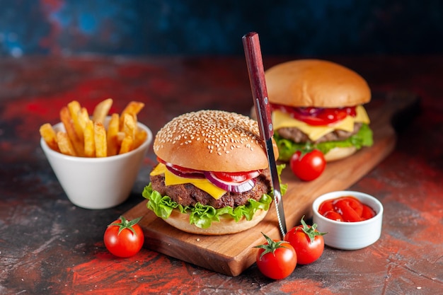 正面図まな板の上のフライドポテトとおいしい肉のチーズバーガー暗い背景ファーストフードの食事スナックディナーディッシュサンドイッチ