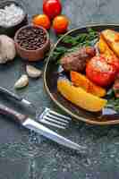 Free photo front view of delicious meat cutlets baked with potatoes and tomatoes on a black plate cutlery set spices garlics tomatoes on green black mixed colors background