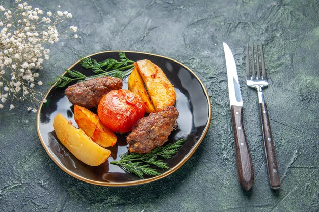 黒のプレートカトラリーでジャガイモとトマトで焼いたおいしい肉のカトラリーの正面図は、緑と黒の混合色の背景に白い花を設定します