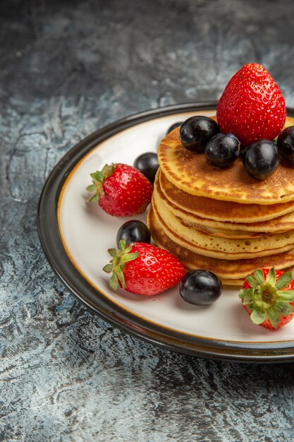 Вид спереди вкусные блины с фруктами и ягодами на темном полу торт фруктовый десерт