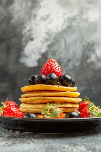 Вид спереди вкусные блины с фруктами и ягодами на темной поверхности фруктовый торт десерт
