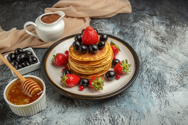 Front view delicious pancakes with honey and fruits on light surface sweet fruit cake