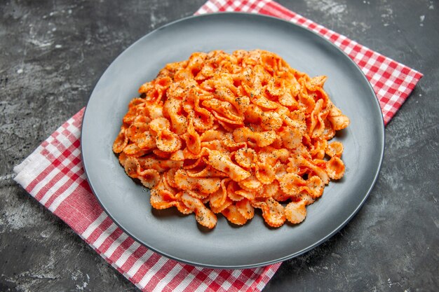 暗い背景に赤い剥ぎ取られたタオルで夕食の黒い皿においしいパスタの食事の正面図