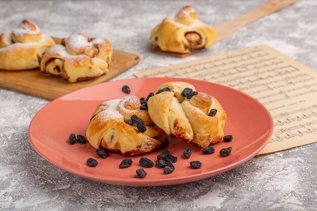 Front view delicious pastries with filling inside plate along with dried fruits on white table, sweet sugar cake bake pastry