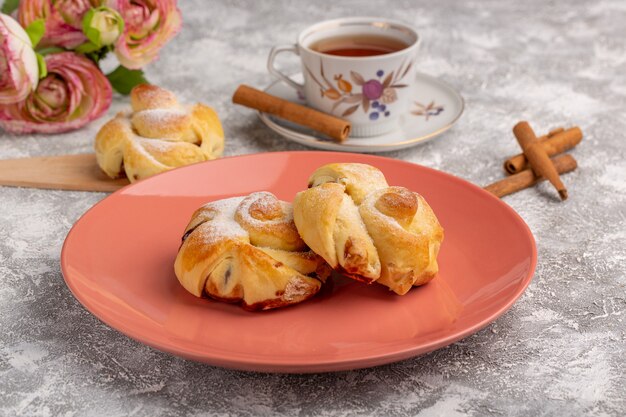 Front view delicious pastries with filling inside plate along with tea and cinnamon on the white table, cake bake pastry fruit