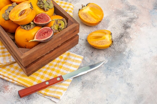 Front view delicious persimmons and cut figs in wood box yellow kitchen towel a knife on nude free space