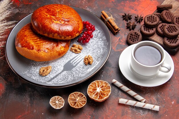 Front view delicious pies with cup of tea on the dark table sweet pie pastry cake